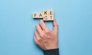 Hand moving 2 scrabble cubes to change the word "fact" to "fake"