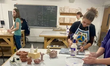 Students working in clay with some of their creations displayed on a table.