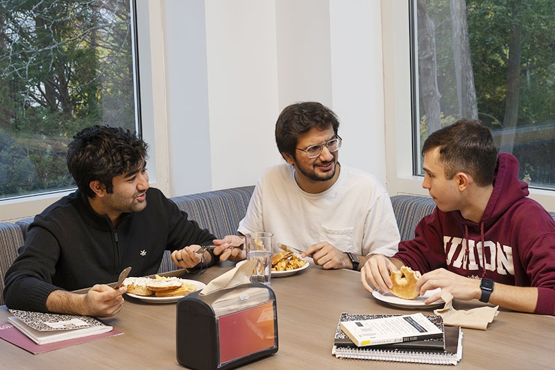  Three students at a dining table enjoying a lively conversation over a delicious meal.